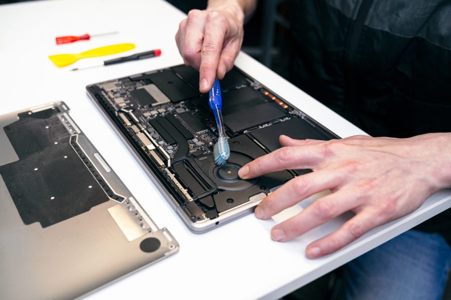 Technician's hands using a brush on a laptop's motherboard for cleaning.