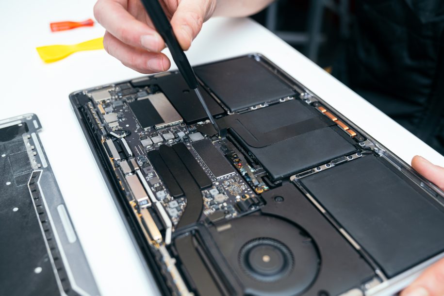 Unrecognizable expert's hands using a tool to fix or upgrade the complex internal hardware of an open laptop on a workbench.