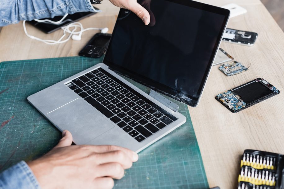 Cropped view of repairman holding damaged laptop with blank screen on workplace with disassembled