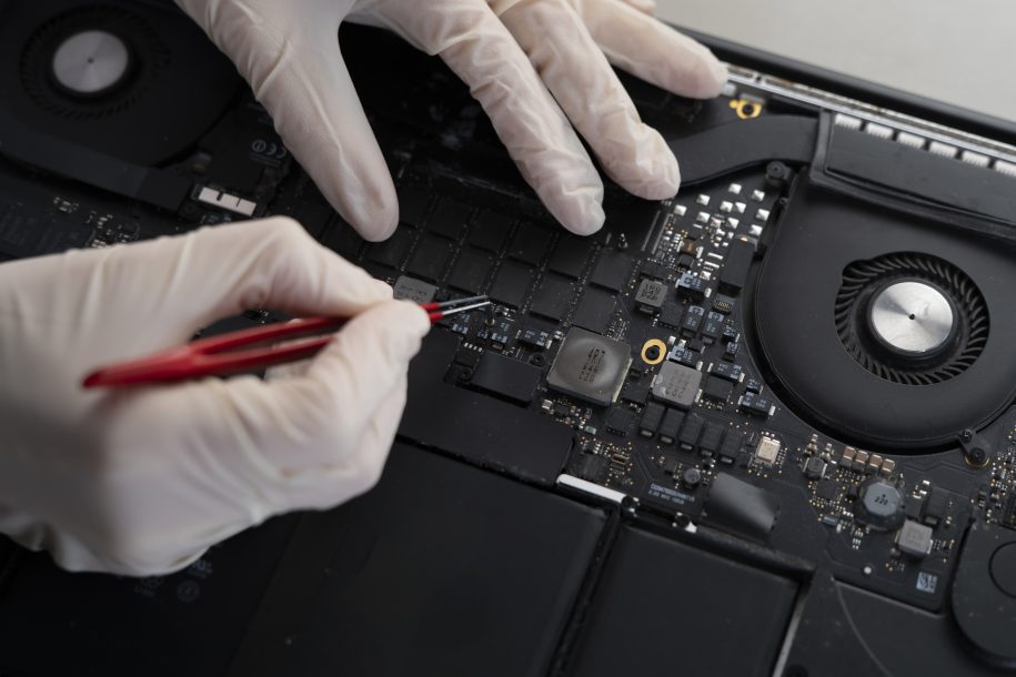 a computer fixing service, master with tweezers repair laptop in the workshop